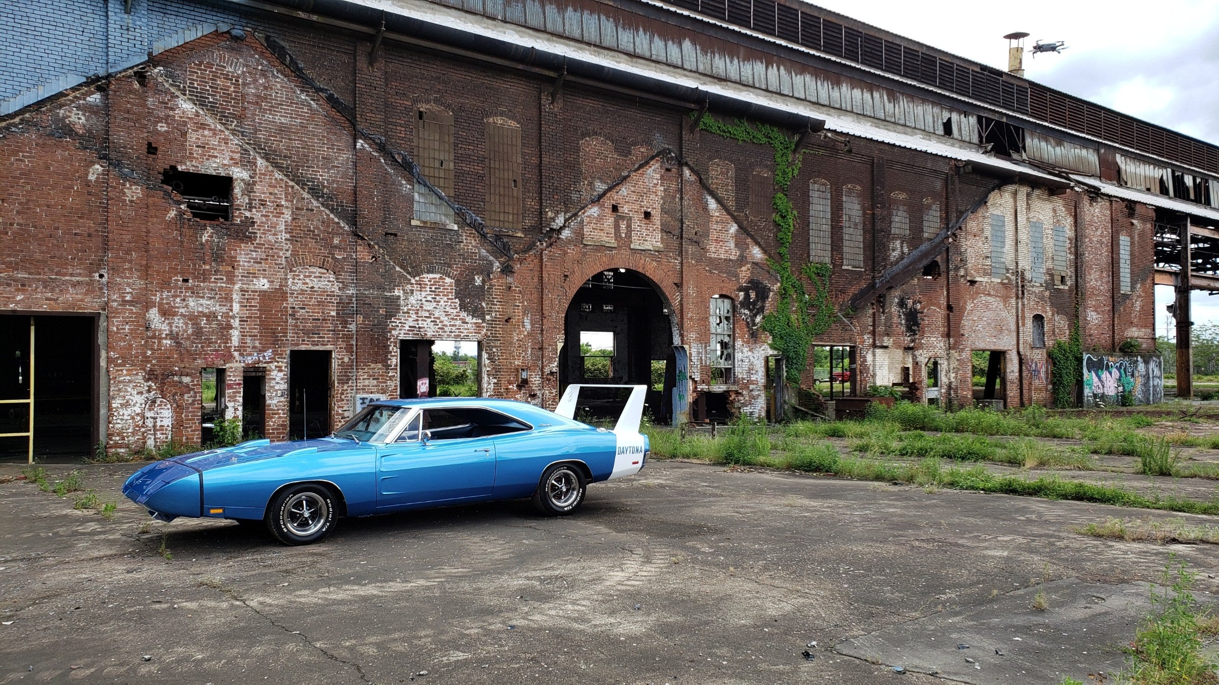 A blue 1969 Dodge Charger Daytona parked in front of the historic brick factory