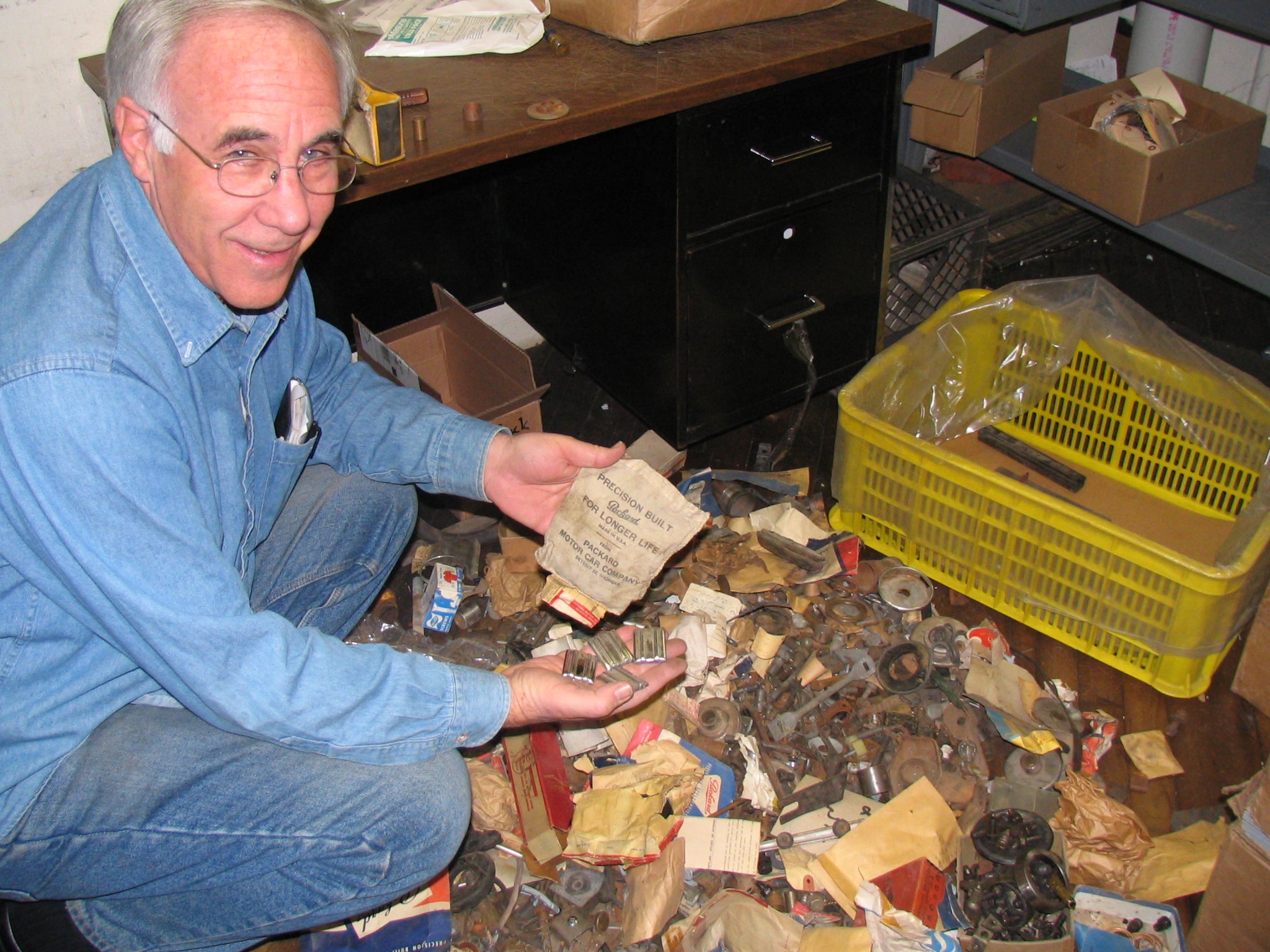 Fred Kanter holding a New Old Stock Packard parts envelope amid boxes of vintage inventory